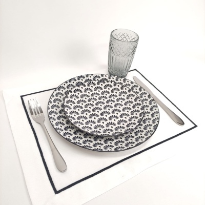 Conjunto de jantar com pratos de cerâmica com padrão de folhas pretas, copo de vidro e talheres sobre toalha branca