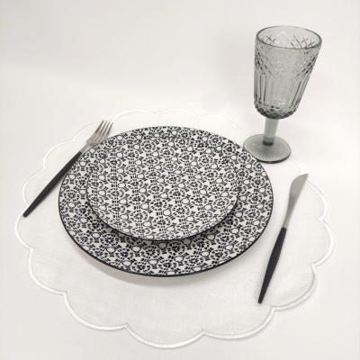 Conjunto de prato, talheres, copo e toalha numa mesa branca.