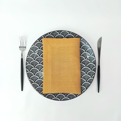 Conjunto para mesa com prato decorado, guardanapo amarelo, garfo e faca com cabos pretos sobre fundo branco