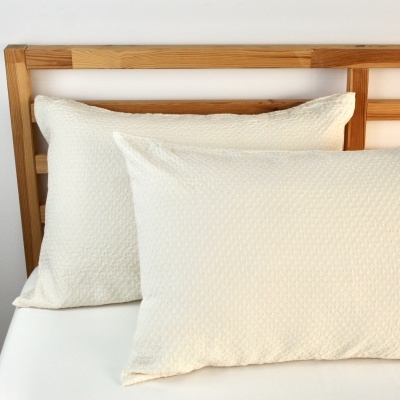 Duas almofadas brancas com textura sobre cama de madeira