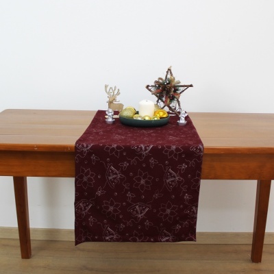 Caminho de mesa bordô com decoração natalícia e velas sobre mesa de madeira