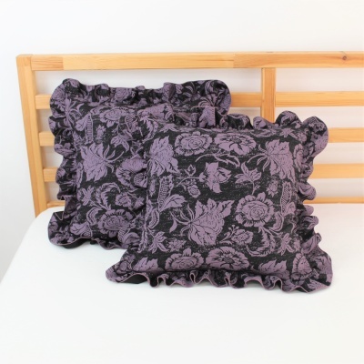 Duas almofadas florais roxas e pretas com bordas frisadas em cama com estrutura de madeira clara