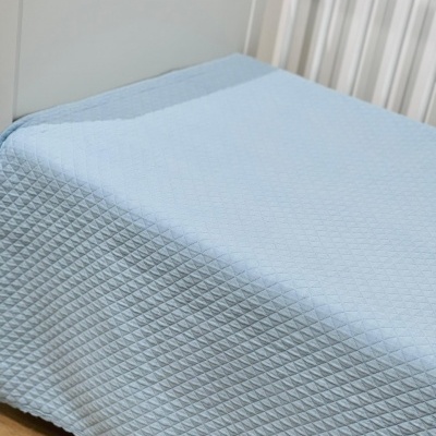 Colcha azul claro acolchoada em cama branca num quarto com chão de madeira.