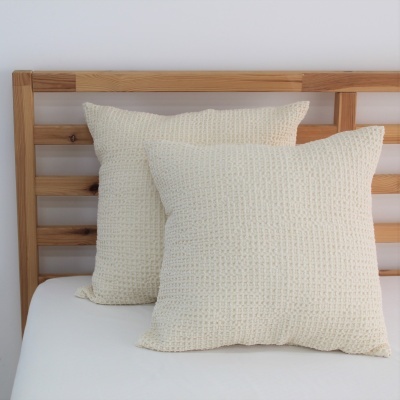 Duas almofadas brancas texturizadas em cama com cabeceira de madeira clara