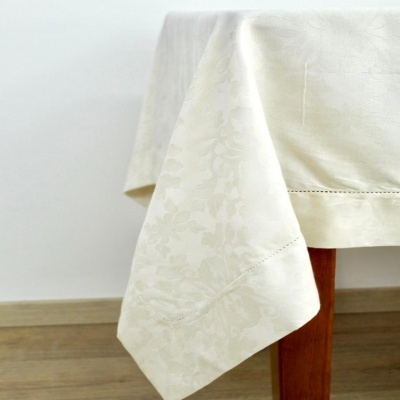 Toalha de mesa branca com padrão floral em relevo e bordado na borda, sobre mesa de madeira