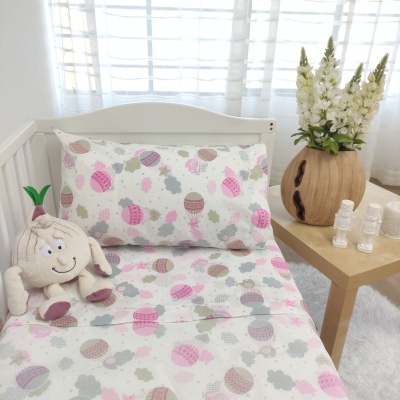 Cama de criança com roupa de cama estampada com balões de ar quente rosa e cinza, boneco de pelúcia, mesa de madeira com vaso e flores brancas