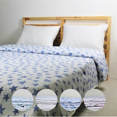 Cobertor com estrelas azuis sobre cama com cabeceira de madeira e almofadas brancas