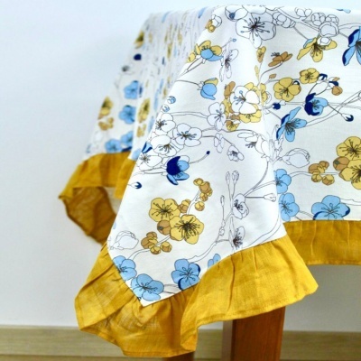Toalha de mesa branca com flores azuis e amarelas e barra amarelo-ocre