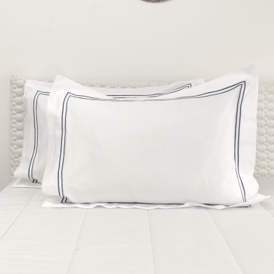 Três almofadas brancas com linha azul escura nas bordas sobre cama branca