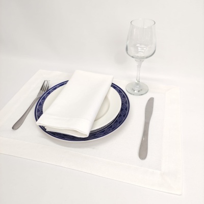 Jogo americano branco com prato branco de borda azul, guardanapo branco, talheres de metal e copo de vinho transparente