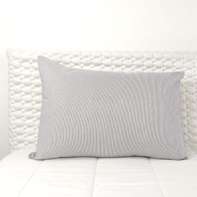 Almofada cinza rectangular sobre cama com cabeceira branca acolchoada