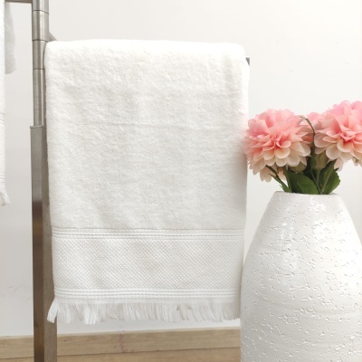 Toalha branca com franjas pendurada ao lado de vaso branco com flores cor-de-rosa