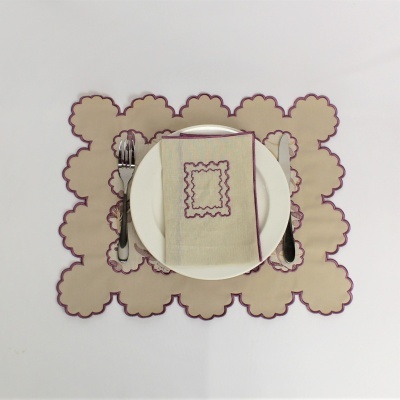 Jogo americano e guardanapo bege com bordas roxas, prato branco e talheres na mesa