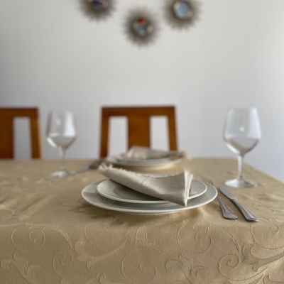 Mesa posta com toalha bege estampada, pratos brancos, talheres, copos de vinho e três relógios na parede