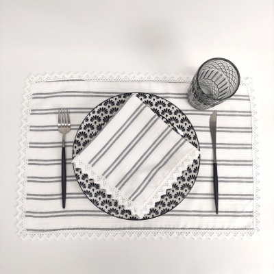 Conjunto de mesa com prato preto e branco, guardanapo e toalhete listrados, talheres pretos e copo decorado.