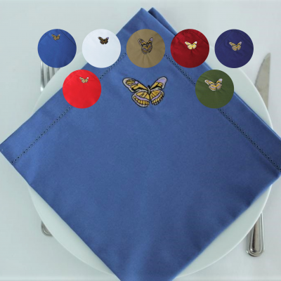 Guardanapo azul com bordado de borboleta sobre prato branco com talheres