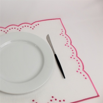 Prato branco cerâmico sobre guardanapo branco com bordado rosa e faca com cabo preto.