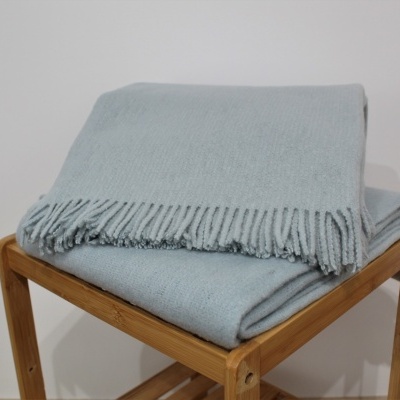 Dupla manta cinza claro com franjas sobre banco de madeira