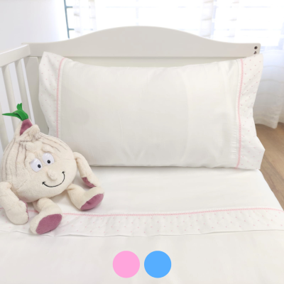 Roupa de cama branca com detalhes cor-de-rosa e peluche de alho sentado num berço branco