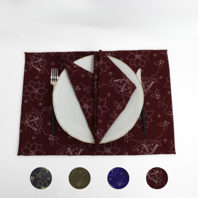Jogo americano bordeaux com padrões florais e guardanapo dobrado, talheres, e outros jogos americano coloridos ao lado.