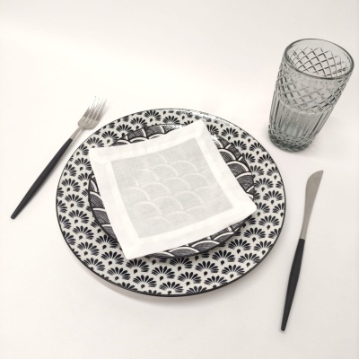 Conjunto de mesa com pratos cerâmicos padrões preto e branco, guardanapo, talheres e copo de vidro.