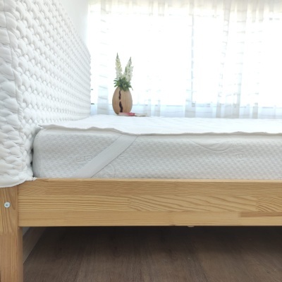 Cama de madeira clara com colchão branco e cabeceira branca acolchoada
