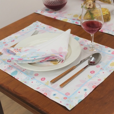 Mesa posta com individual floral, prato branco, guardanapo, talheres de cabo de madeira e taça com vinho tinto