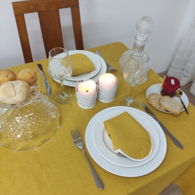 Mesa de jantar posta com toalha amarela, pratos brancos, velas acesas e copos de vidro