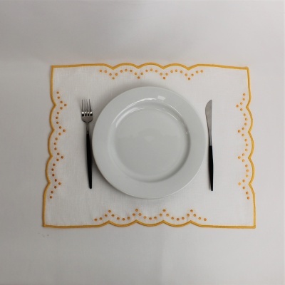 Posto de mesa branco com borda amarela, prato branco redondo, garfo e faca com cabos pretos