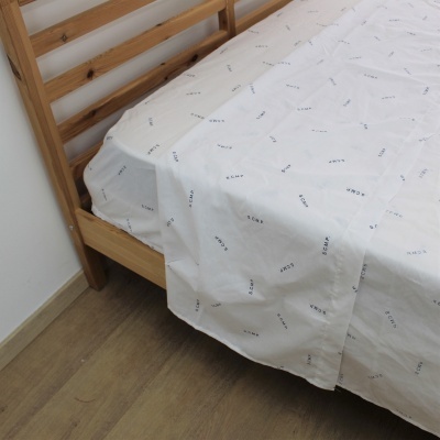 Cama de madeira com lençol branco estampado com texto azul