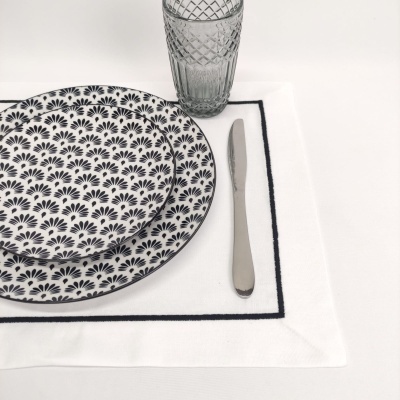 Conjunto de pratos com padrão preto, copo de vidro texturizado, faca e toalha branca com borda preta