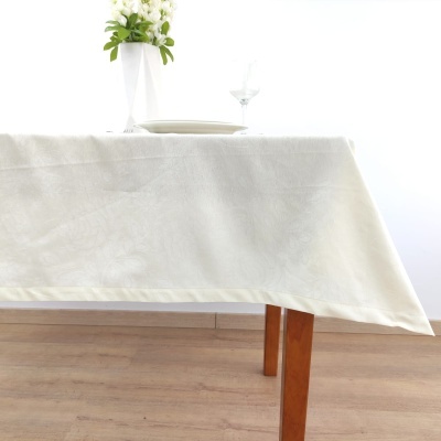 Toalha de mesa branca com padrão floral subtil numa mesa de madeira clara com decoração simples ao fundo