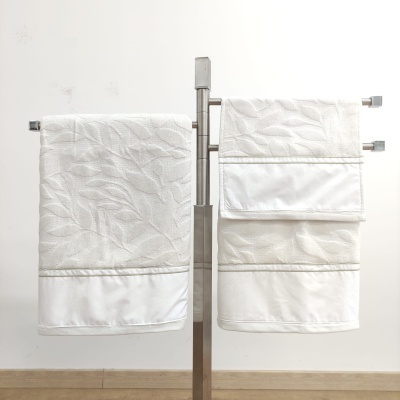 toalhas brancas com padrão de folhas em relevo penduradas num suporte metálico prateado