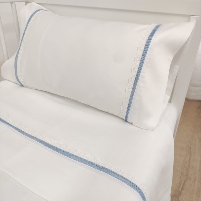 Jogo de cama branco com bordado branco e faixa azul em cama branca