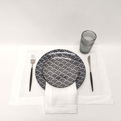 Conjunto de mesa com prato decorado, talheres pretos, guardanapo branco e copo de vidro