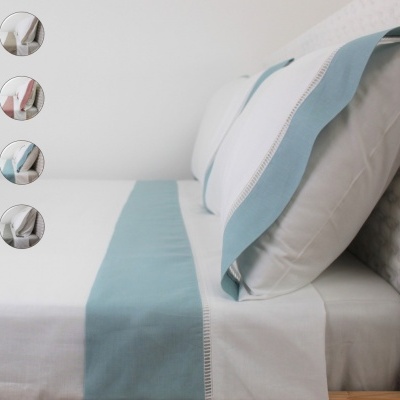 Roupa de cama branca com bordado azul claro e cabeceira branca com padrão ao fundo