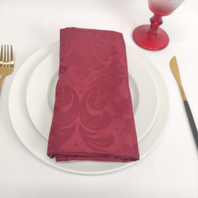 Guardanapo bordô com padrão em prato branco, talheres dourados e copo vermelho