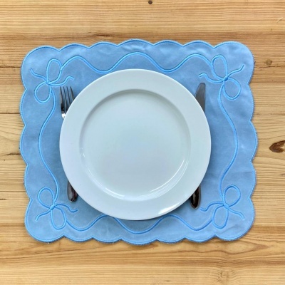 Jogo americano azul claro com prato branco, garfo e faca sobre mesa de madeira