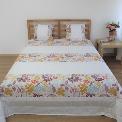 Conjunto cama branco com padrões florais coloridos, cabeceira de madeira clara, mesa lateral com vaso de flores.