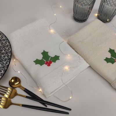 Toalhas de mão com bordado natalino, copos, talheres e luzes decorativas sobre mesa clara