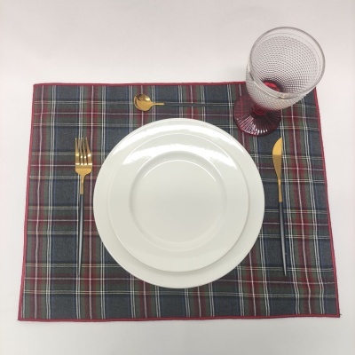 Mesa posta com pratos brancos, talheres dourados, placemat xadrez e copo com pé vermelho.