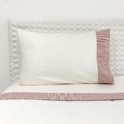 Travesseiro branco com borda rosa listrada numa cama branca com cabeceira estofada