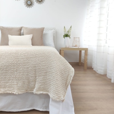 Cama com colcha bege e almofadas neutras junto a mesa de cabeceira com decoração