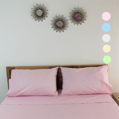 Cama com lençóis cor-de-rosa e três espelhos decorativos circulares na parede branca