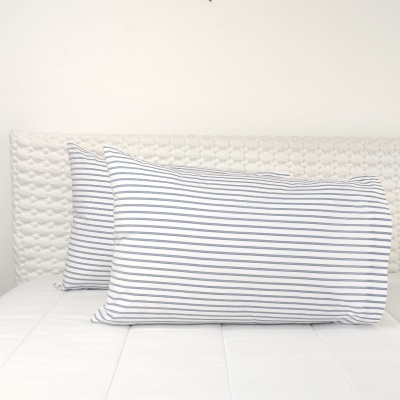 Duas almofadas riscas azuis e brancas numa cama com cabeceira branca revestida.