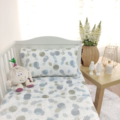 Cama de criança branca com roupa de cama estampada e almofada decorativa junto a mesa com decoração