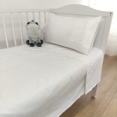 Cama de bebé branca com roupa de cama branca bordada e peluche cinzento