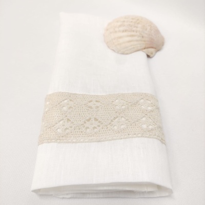 Guardanapo branco com faixa de renda bege e concha clara em fundo branco