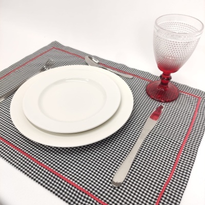 Conjunto de louça com pratos brancos, talheres metálicos, copo com base vermelha e toalhete xadrez preto, branco e vermelho