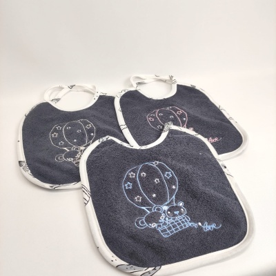 Três babetes cinzentos com bordas brancas e bordados de balões e ursos.